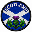Round 80mm Scotland embroidered patch showing a purple and green thistle below a white Saltire on blue, with SCOTLAND lettering, finished with a black border.