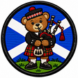 Round 80mm embroidered patch showing a teddy bear playing bagpipes in a red tartan kilt against a blue and white Saltire, framed by a black border.