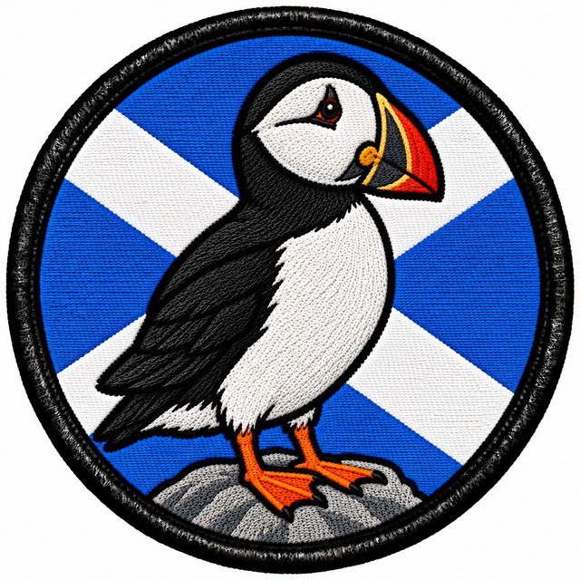 Round 80mm embroidered patch showing a black and white puffin with an orange beak and feet standing on a rock against a Saltire, framed by a black border.