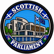 Round 80mm embroidered patch showing a stylised Scottish Parliament building with Scottish and European flags, thistles and SCOTTISH PARLIAMENT lettering, framed by a black border.