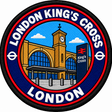 Round 80mm embroidered patch showing a stylised King's Cross station facade with twin arches, a clock tower and a railway sign, finished with a black border.
