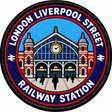 Round 80mm embroidered patch showing a stylised Liverpool Street station facade with red brick towers, a central clock and LONDON LIVERPOOL STREET RAILWAY STATION lettering, finished with a black border.