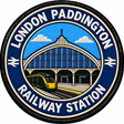 Round 80mm embroidered patch showing a green passenger train beside a stylised Paddington station facade with an arched glass roof, finished with a black border.