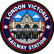 Round 80mm embroidered patch showing the Victoria station entrance and clock, with people outside and LONDON VICTORIA RAILWAY STATION lettering, finished with a black border.