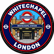 Round 80mm embroidered patch showing the Whitechapel station entrance beneath an Underground roundel, with WHITECHAPEL and LONDON lettering and red trim, finished with a black border.